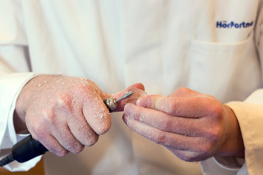 Ein Hörakustiker schleift ein Hörgerät präzise in einer Fachwerkstatt zurecht.